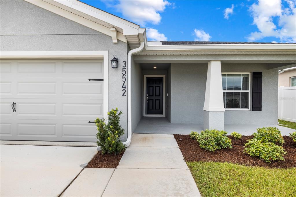 A gray house exterior features a garage, a front door, and a concrete walkway — 35542 BELLINGTON BOULEVARD, ZEPHYRHILLS, FL