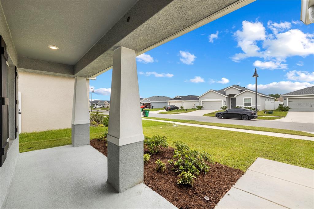 A view from a covered front porch looking out toward a suburban street and houses — 35542 BELLINGTON BOULEVARD, ZEPHYRHILLS, FL