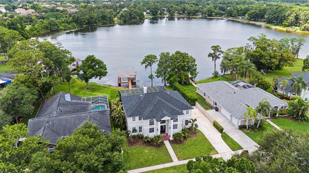 An aerial view shows a two-story house with a dark roof situated beside a lake — 15004 MAURINE COVE LANE, ODESSA, FL