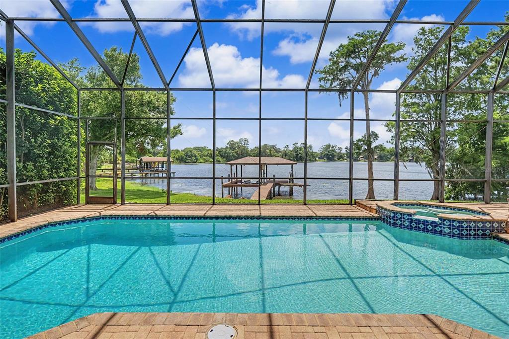 A screened-in swimming pool and hot tub overlook a lake with a private boat dock — 15004 MAURINE COVE LANE, ODESSA, FL