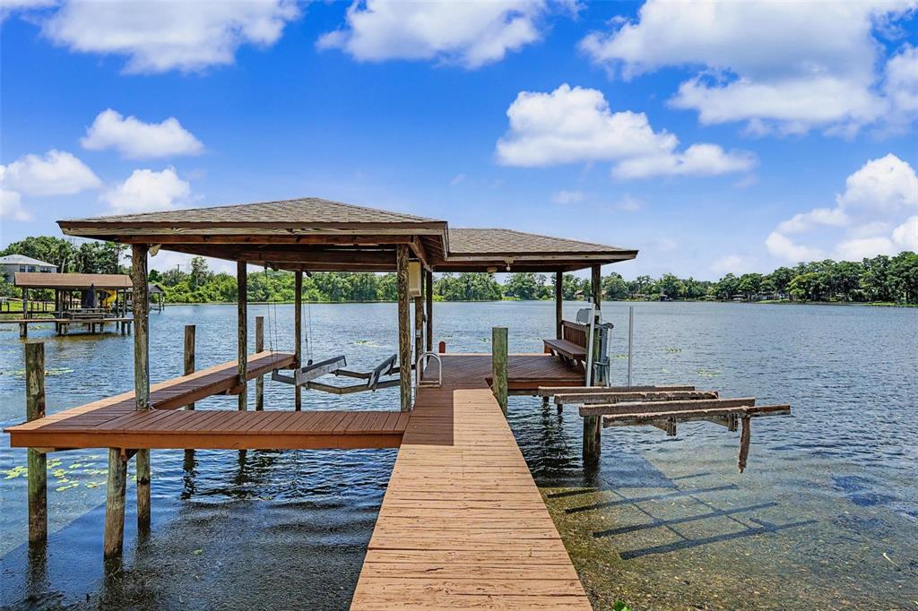 A wooden boat dock with a covered seating area extends over a calm lake — 15004 MAURINE COVE LANE, ODESSA, FL