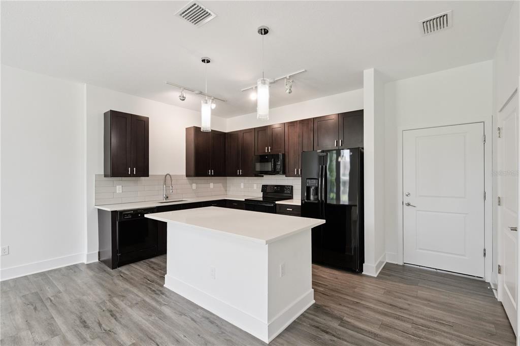 A kitchen features dark wood cabinets, black appliances, a white island, and light wood flooring — 1841 HOUSTON STREET, KISSIMMEE, FL