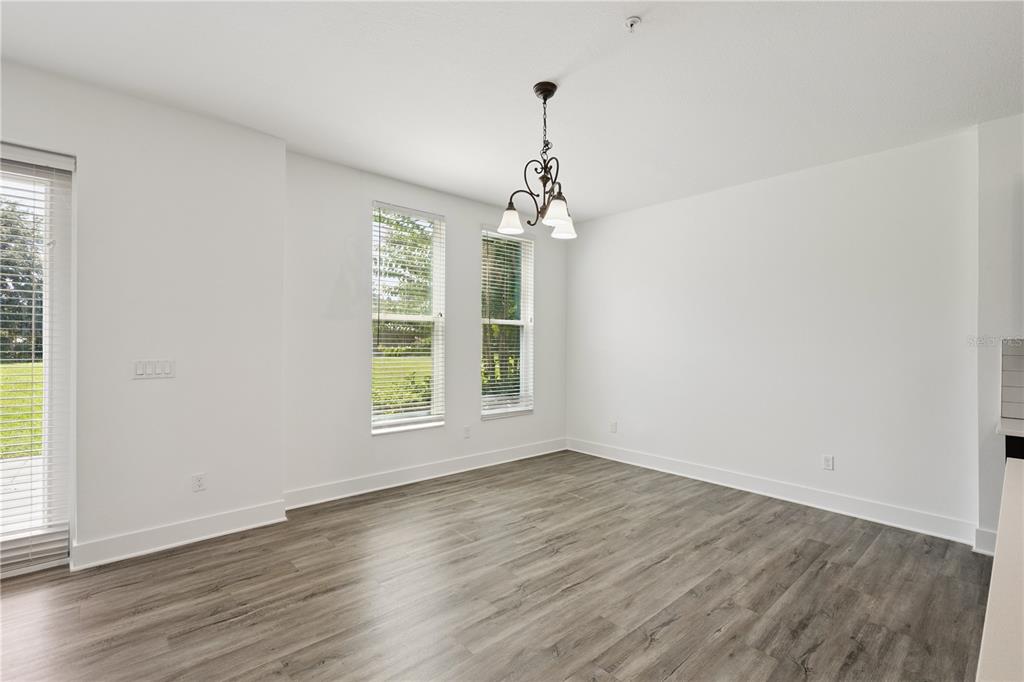 An empty dining room features white walls, wood-look flooring, a chandelier, and two windows — 1841 HOUSTON STREET, KISSIMMEE, FL