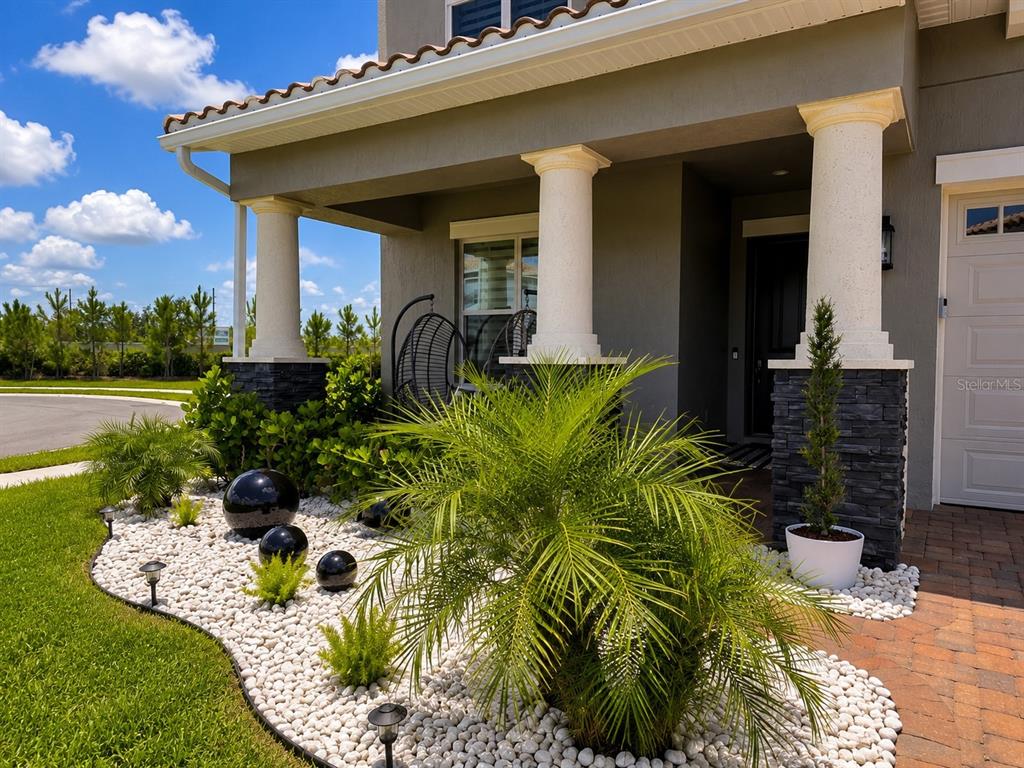 The exterior of a house features a covered porch with stone columns and landscaping — 13207 AYLESBURY STREET, ORLANDO, FL