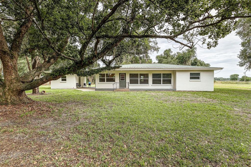 A single-story white house with a metal roof sits behind a large, sprawling oak tree — 5256 KNIGHTS STATION ROAD, LAKELAND, FL