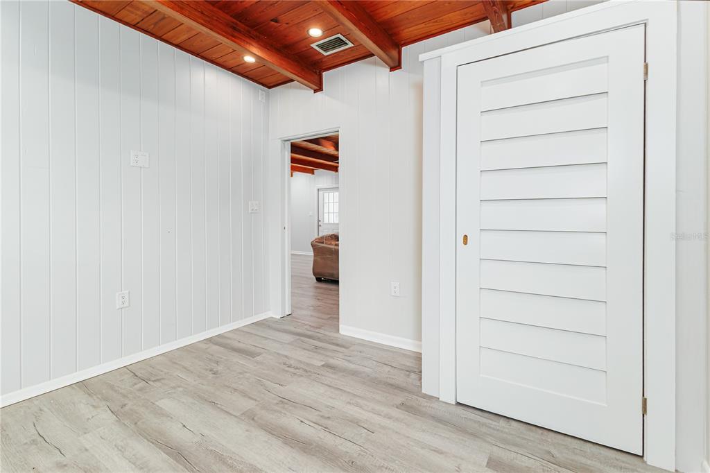 A room with white vertical paneled walls, wood-beamed ceilings, light flooring, and a white door — 5256 KNIGHTS STATION ROAD, LAKELAND, FL