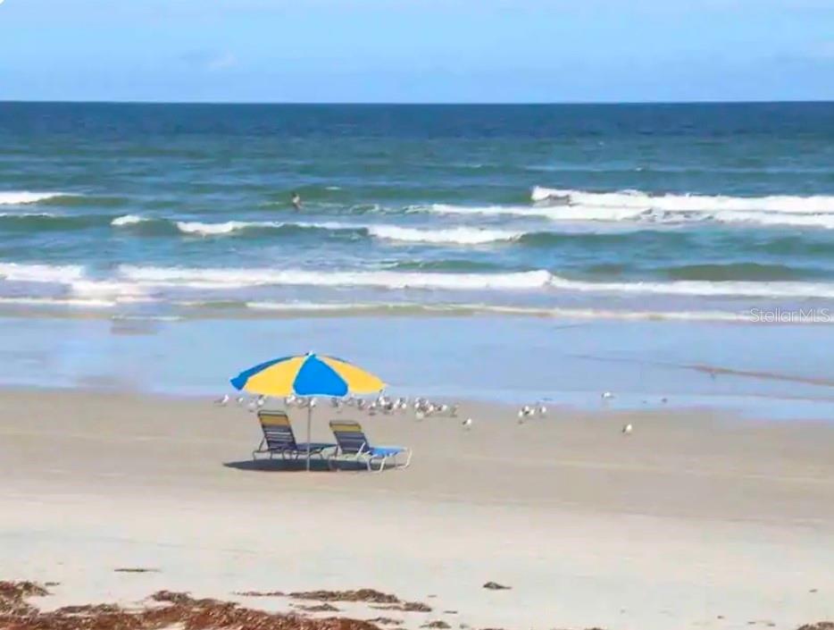 A beach scene features a blue and yellow umbrella over two chairs on the sand — 701 S ATLANTIC AVENUE UNIT 520, DAYTONA BEACH, FL