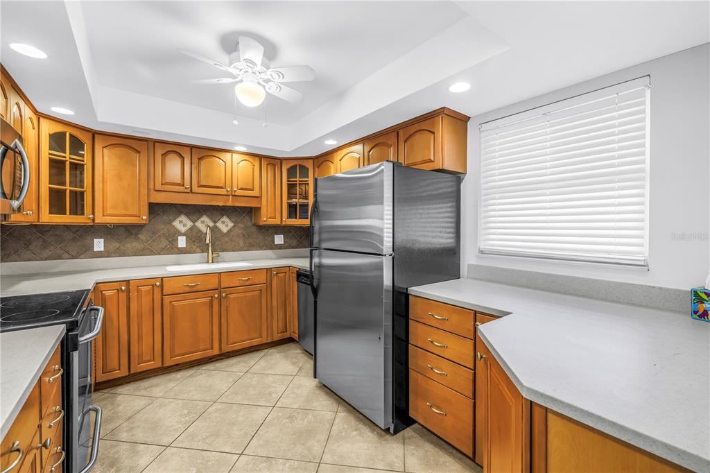 A kitchen features wood cabinets, stainless steel appliances, tile flooring, and a window with blinds — 5108 BRITTANY DRIVE S UNIT 405, ST PETERSBURG, FL
