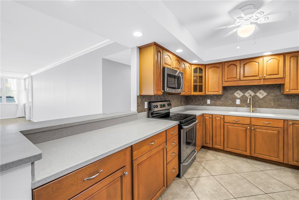 A kitchen features wood cabinets, gray countertops, a stainless steel stove, and tile flooring — 5108 BRITTANY DRIVE S UNIT 405, ST PETERSBURG, FL