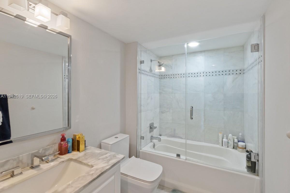A bathroom features a white vanity, a toilet, and a glass-enclosed shower-tub combination — 90 Alton Rd # 807, Miami Beach FL 33139, MIAMI BEACH, FL