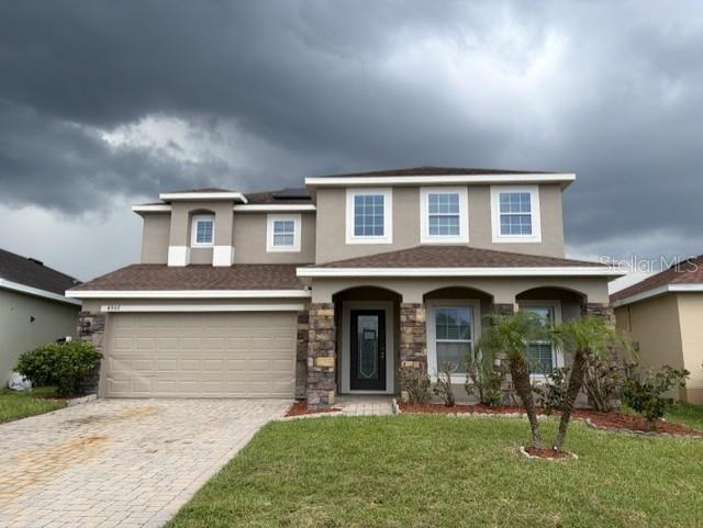 A two-story house with a tan stucco exterior, stone accents, and a paved driveway — 4907 ROCKVALE DR., KISSIMMEE, FL