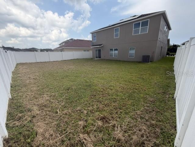 A fenced backyard with grass leads to the rear exterior of a two-story house — 4907 ROCKVALE DR., KISSIMMEE, FL