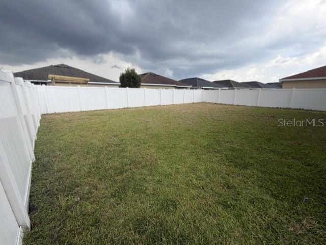 A fenced-in backyard with a grass lawn under a cloudy sky — 4907 ROCKVALE DR., KISSIMMEE, FL