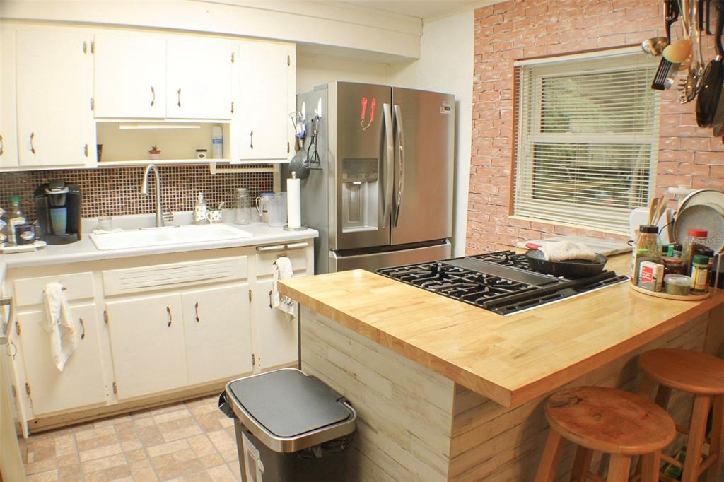 A kitchen with white cabinets, a stainless steel refrigerator, a butcher block island, and brick-patterned walls — 1405 28TH STREET NW, WINTER HAVEN, FL