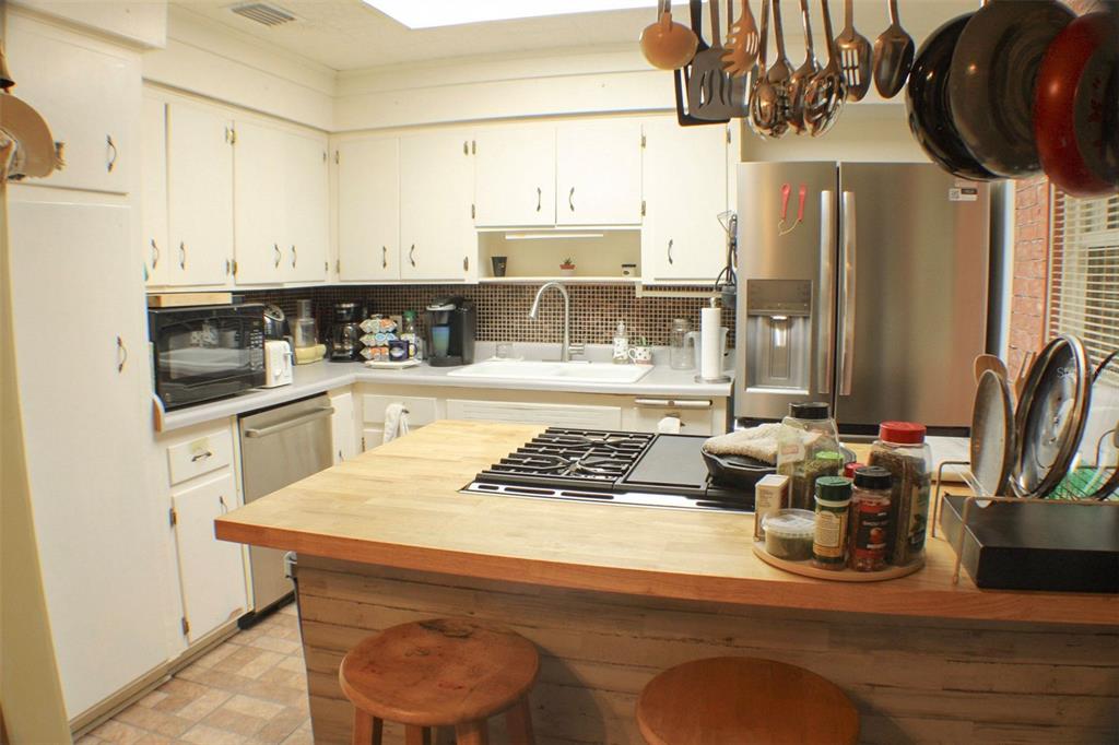A kitchen features white cabinets, a wood-topped island with a cooktop, and stainless steel appliances — 1405 28TH STREET NW, WINTER HAVEN, FL