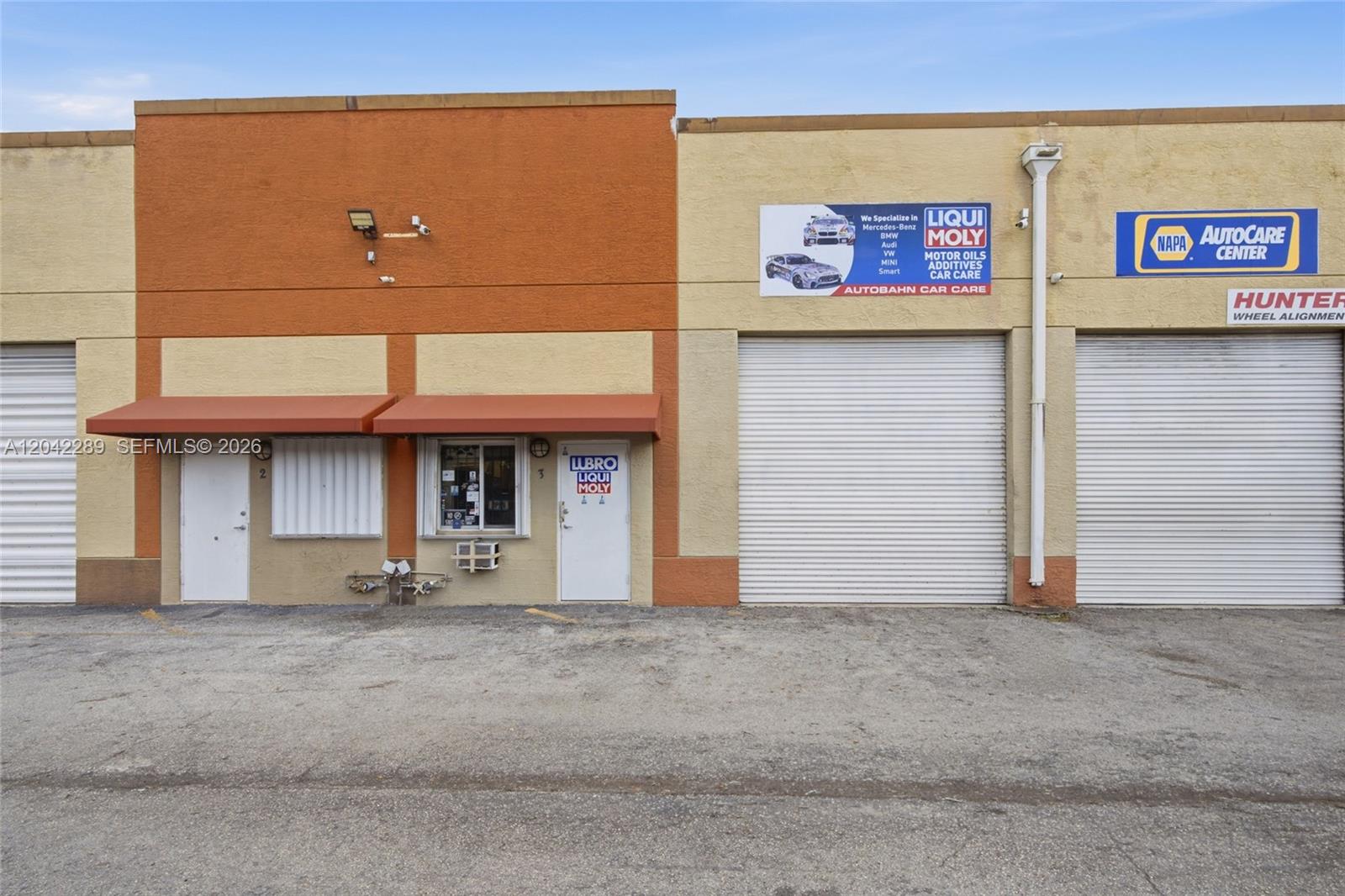 The exterior of a commercial building features two roll-up garage doors and a central entrance — 11950 SW 144th Ct, Miami FL 33186, MIAMI, FL