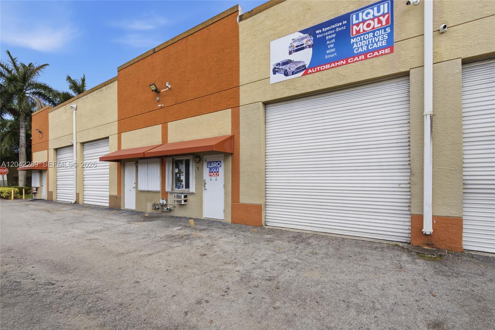 The exterior of a commercial warehouse building features multiple roll-up garage doors and signage — 11950 SW 144th Ct, Miami FL 33186, MIAMI, FL