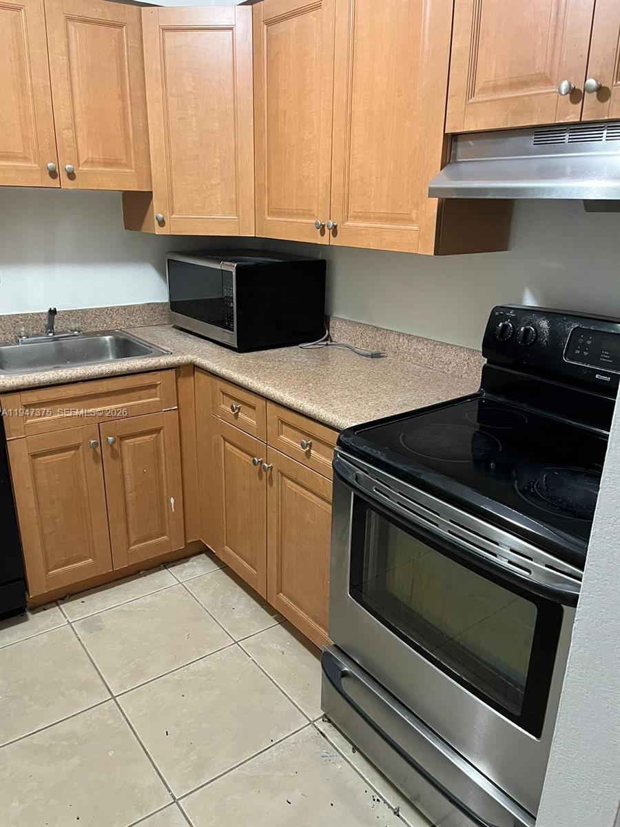 A kitchen features wood cabinets, a stainless steel stove, and a black microwave on countertops — 5221 Geneva Way # 302, Doral FL 33166, DORAL, FL