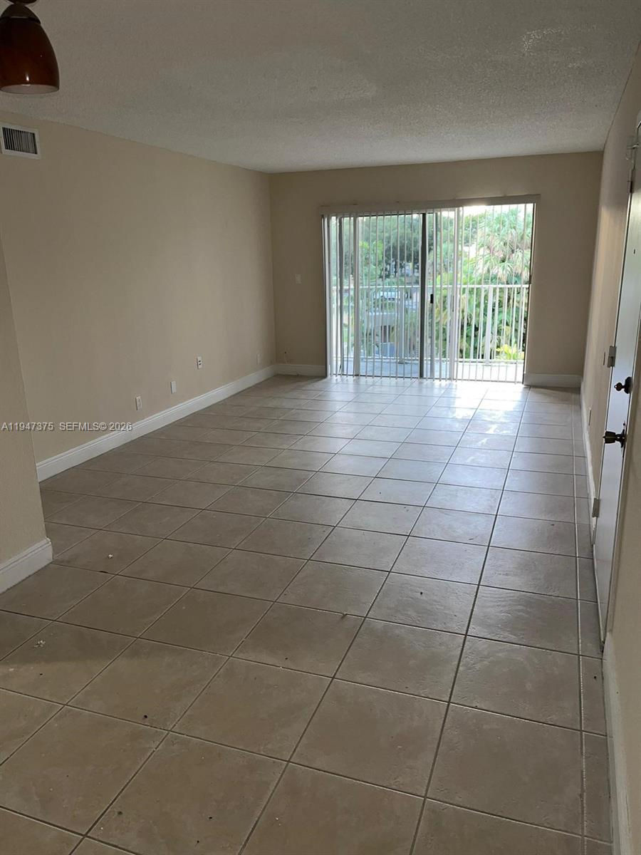 An empty living room features beige walls, light-colored floor tiles, and a sliding glass door — 5221 Geneva Way # 302, Doral FL 33166, DORAL, FL