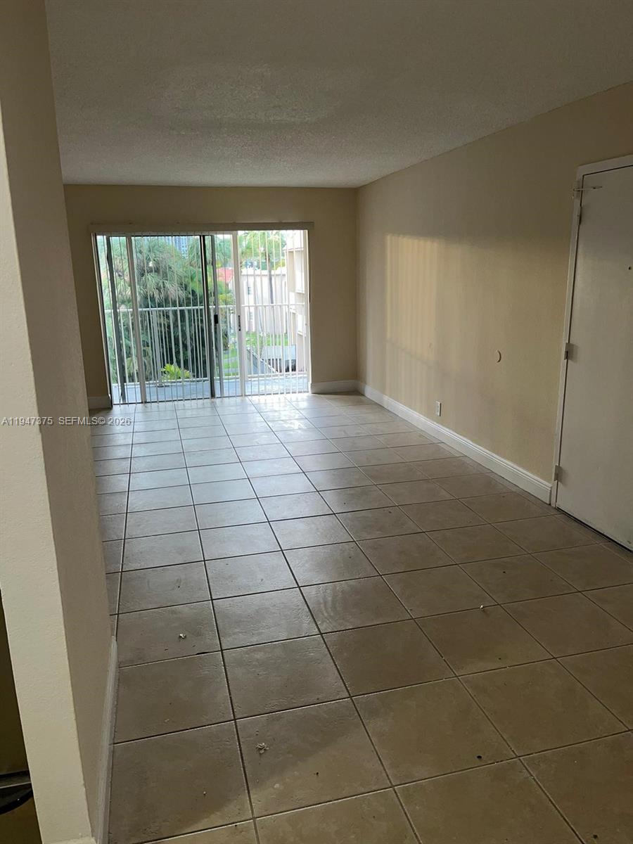 An empty living room features beige tile flooring, light-colored walls, and a sliding glass balcony door — 5221 Geneva Way # 302, Doral FL 33166, DORAL, FL