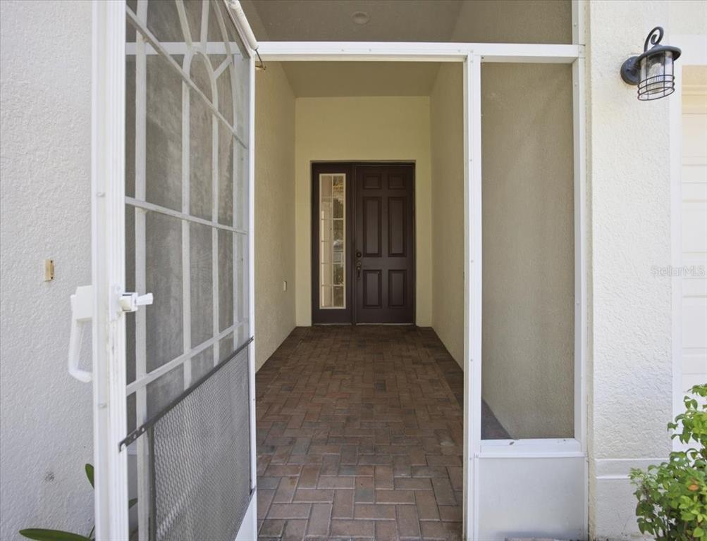 A paved entryway leads to a dark brown front door behind a white screen door — 794 WOLF CREEK STREET, CLERMONT, FL