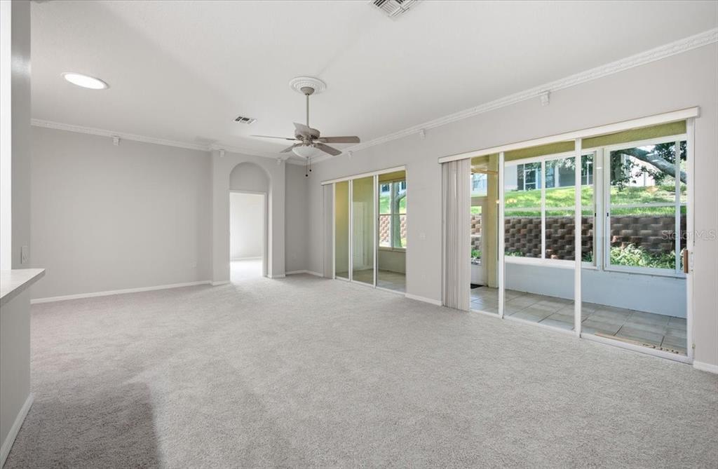 A spacious living room with gray carpeting, a ceiling fan, and large sliding glass doors — 794 WOLF CREEK STREET, CLERMONT, FL