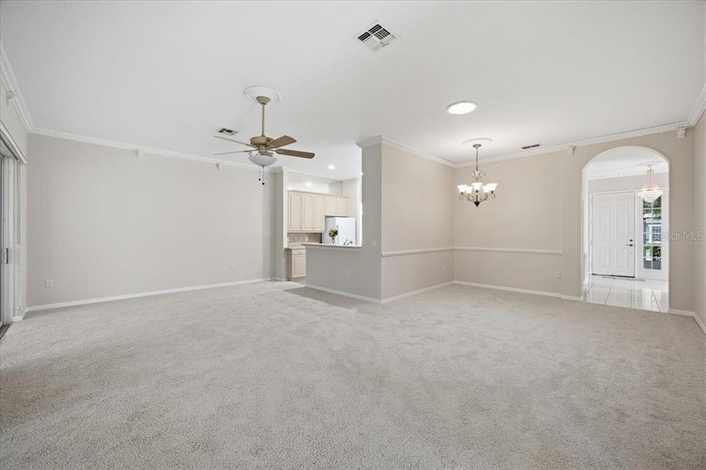 A spacious living room with beige carpet, a ceiling fan, and an arched entryway — 794 WOLF CREEK STREET, CLERMONT, FL