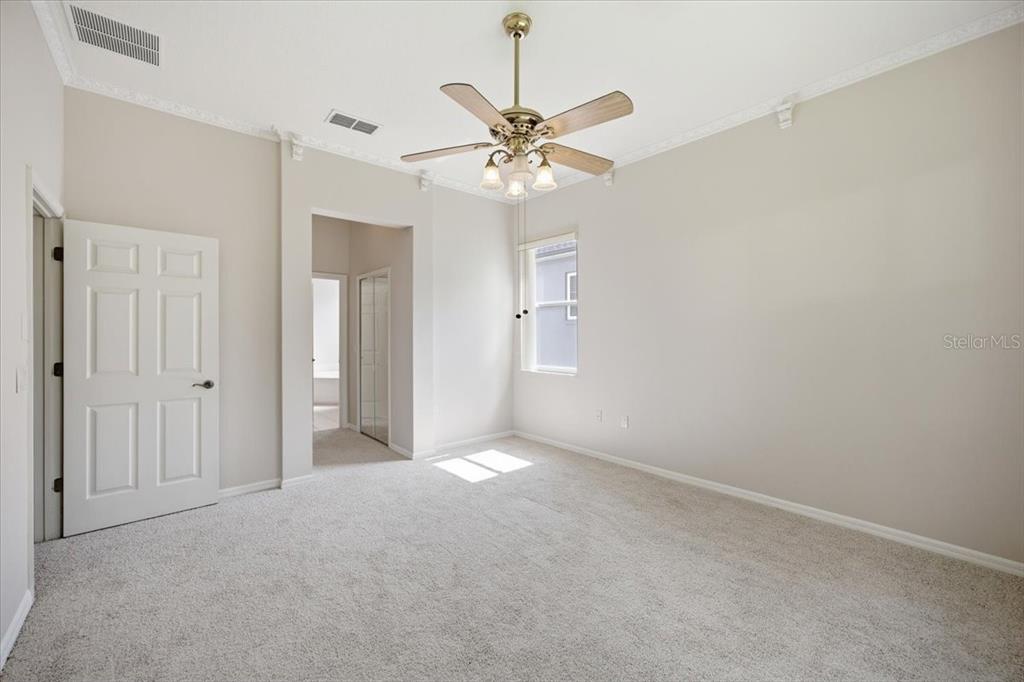 A bedroom with beige walls, light carpeting, a ceiling fan, and an open doorway — 794 WOLF CREEK STREET, CLERMONT, FL
