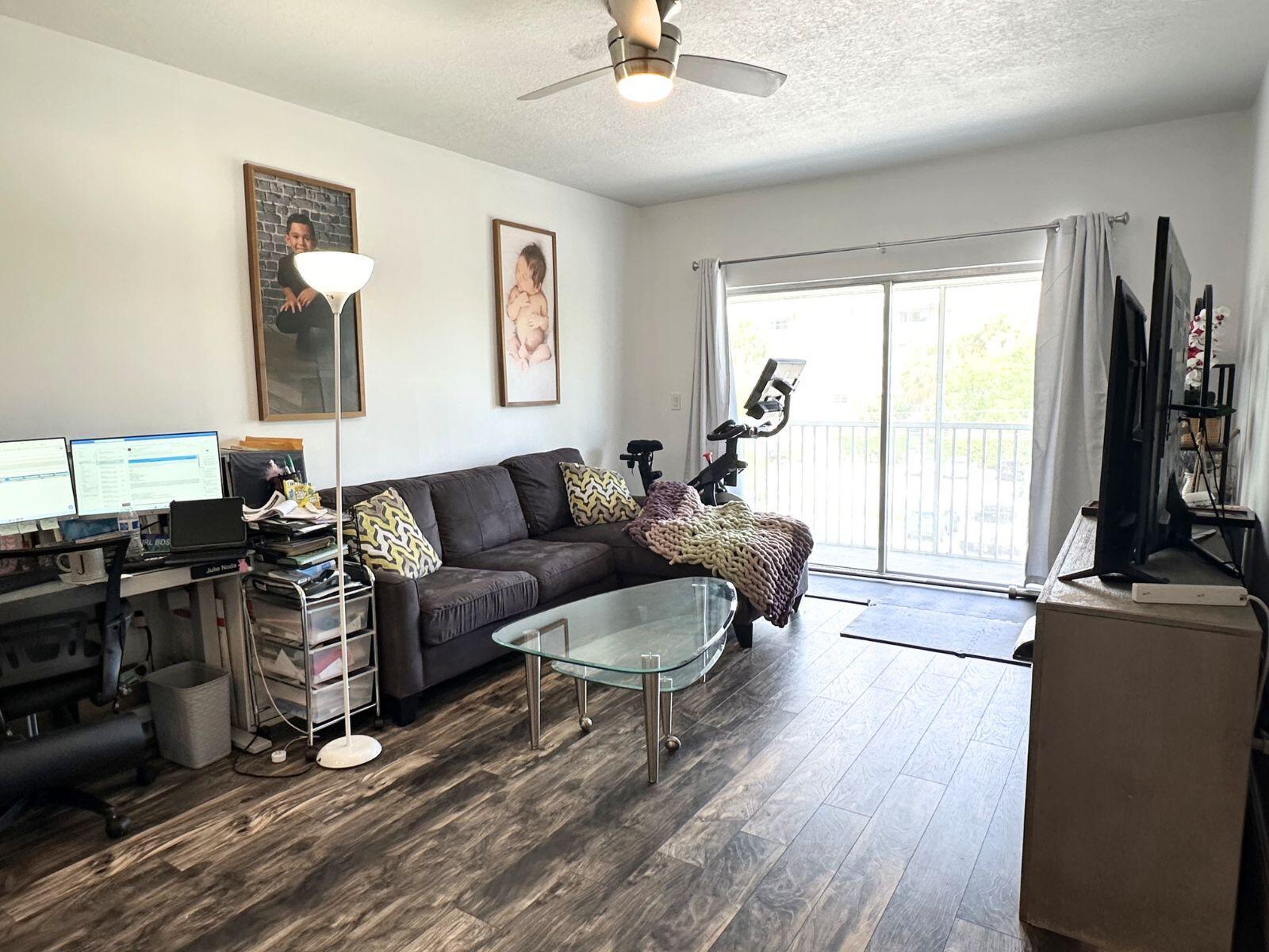A living room with a sectional sofa, glass coffee table, desk, and exercise bike — 50 SW 3rd Avenue # 3020, Boca Raton FL 33432, BOCA RATON, FL
