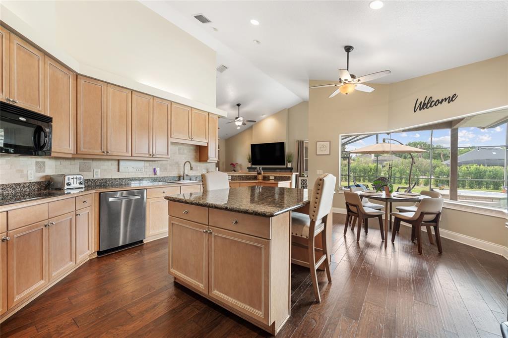 A kitchen with light wood cabinets, granite countertops, a center island, and a dining area — 8612 OLDBRIDGE LANE, ORLANDO, FL