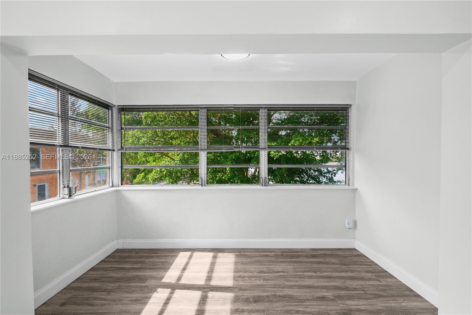 A bright, empty room features light wood-look flooring, white walls, and large corner windows — 245 NE 191st St # 3014, Miami FL 33179, MIAMI, FL