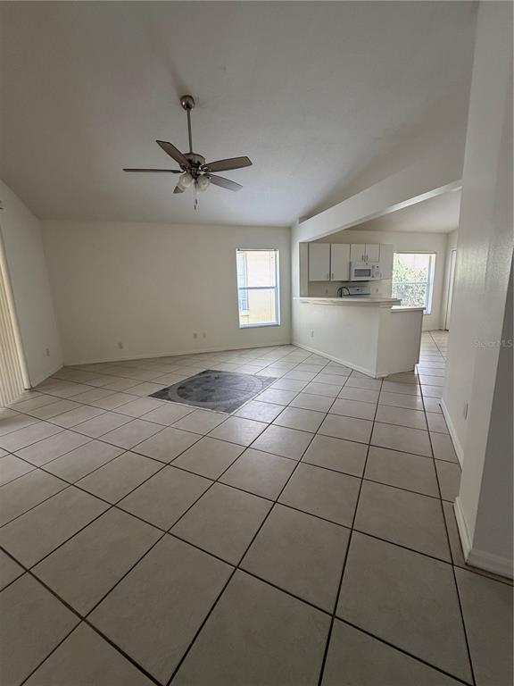 A living room with tile flooring, a ceiling fan, and an open kitchen with white cabinets — 5554 LIGUSTRUM LOOP, OVIEDO, FL