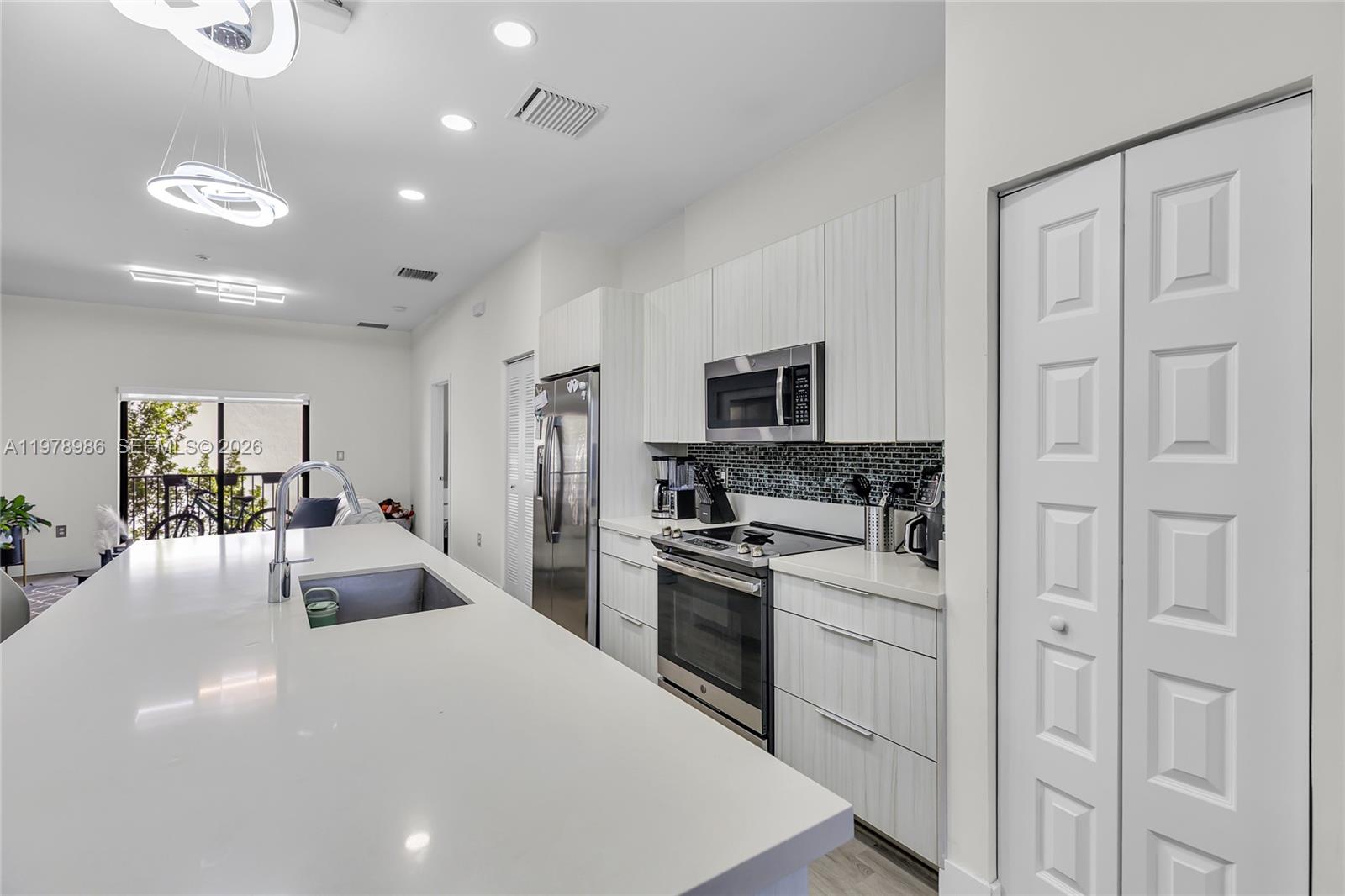A modern kitchen features white cabinetry, stainless steel appliances, and a large quartz island — 7925 NW 104th Ave # 28, Doral FL 33178, DORAL, FL