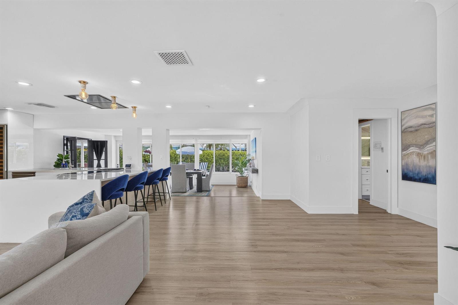 A bright, open-concept living and dining area features white walls, wood-look flooring, and blue barstools — 2917 NE 35th Court, Lighthouse Point FL 33064, LIGHTHOUSE POINT, FL