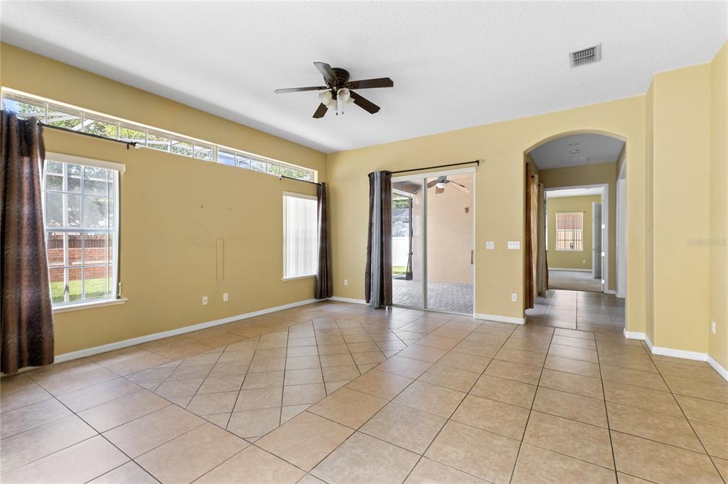 A spacious living room features tan tile flooring, yellow walls, a ceiling fan, and sliding doors — 16407 BRISTOL LAKE CIRCLE, ORLANDO, FL