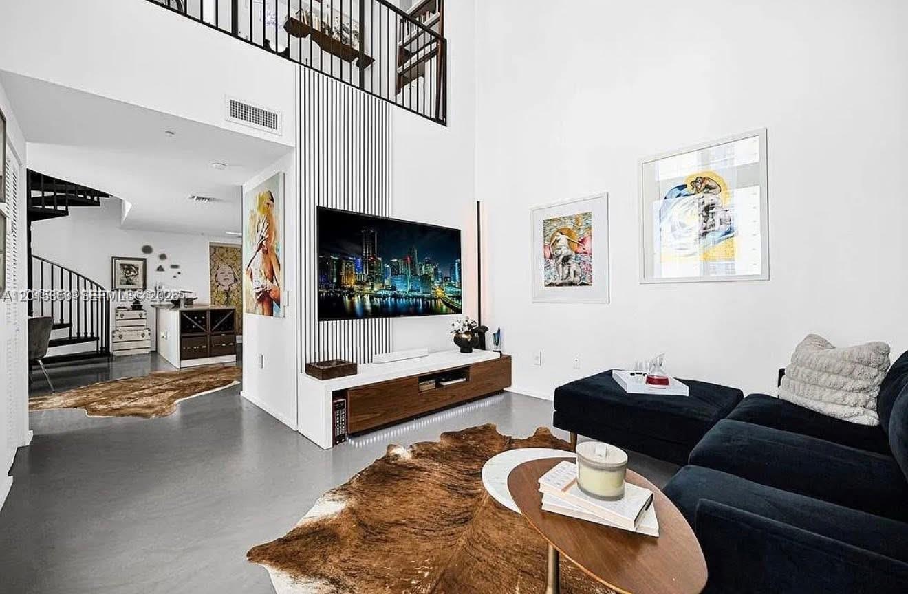 A modern living room features a tall ceiling, a wall-mounted television, and a spiral staircase — 300 S Biscayne Blvd # 1232, Miami FL 33131, MIAMI, FL