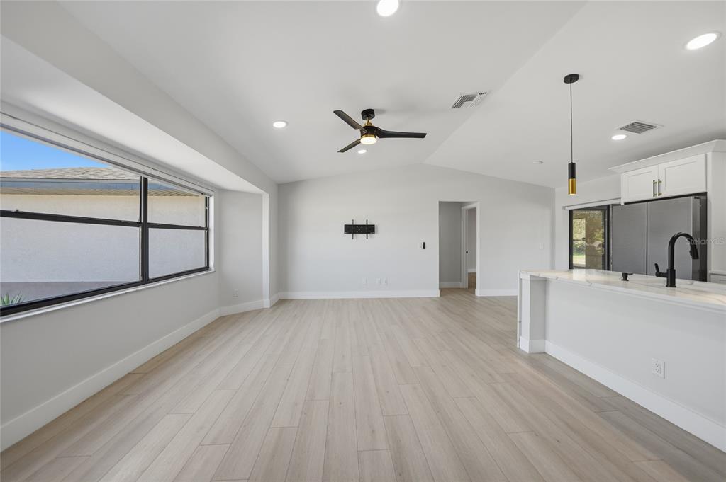 A bright, open-concept living area features light wood-look flooring, a ceiling fan, and a kitchen island — 5009 JODY AVENUE, NORTH PORT, FL
