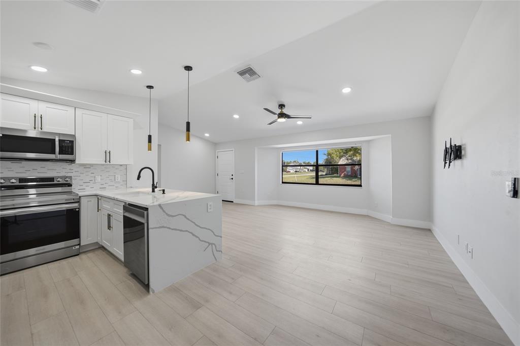 A modern kitchen with white cabinets and a marble-topped island opens into a living area — 5009 JODY AVENUE, NORTH PORT, FL