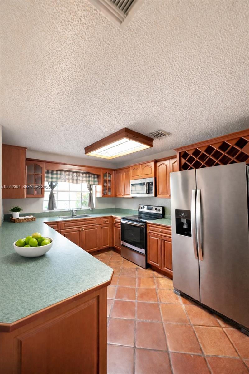 A kitchen features wooden cabinets, green countertops, stainless steel appliances, and terracotta tile flooring — 1045 NW 126th Pl, Miami FL 33182, MIAMI, FL
