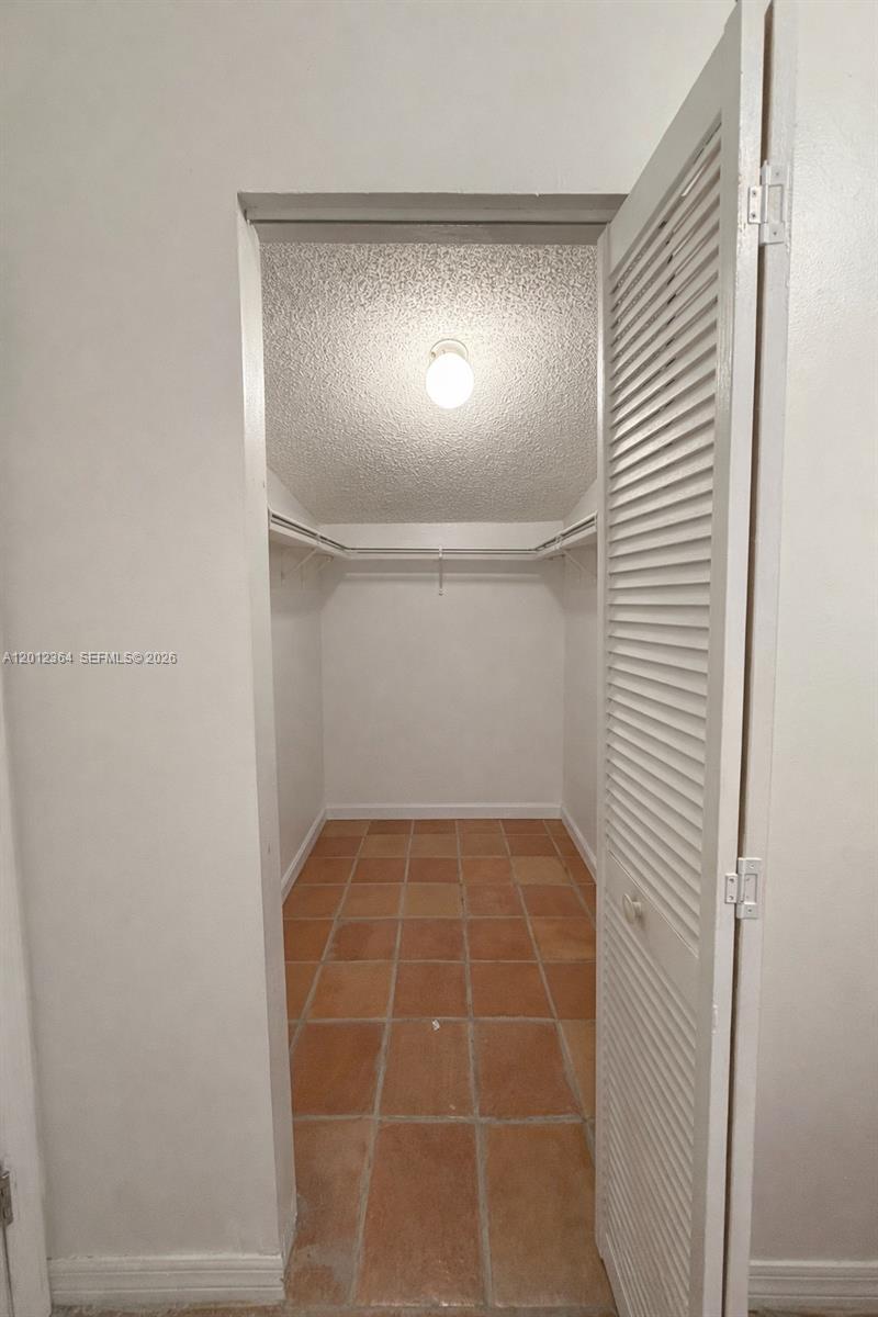 An empty room features terracotta tile flooring, white walls, and a window with blinds — 1045 NW 126th Pl, Miami FL 33182, MIAMI, FL