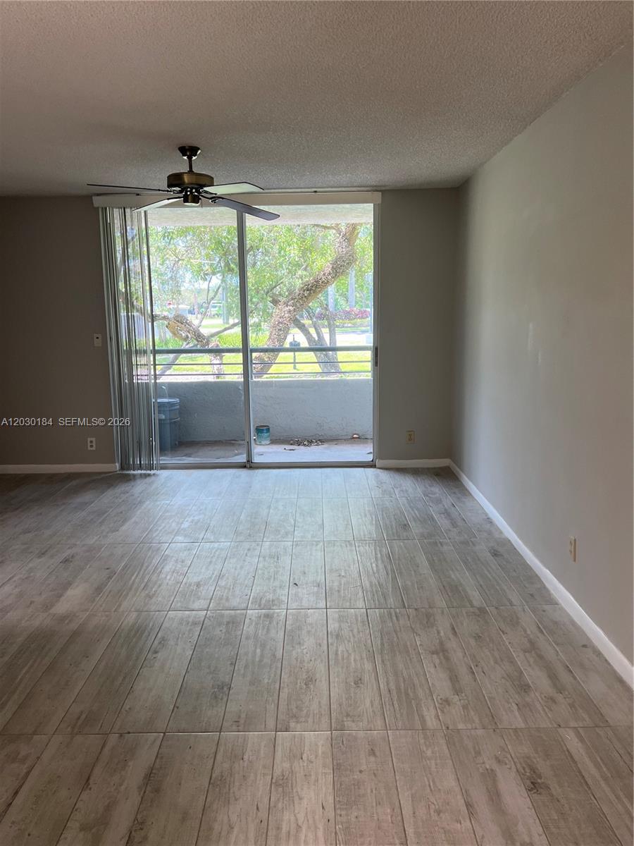 An empty room features light wood-look tile flooring, a ceiling fan, and sliding glass doors — 951 Lyons Rd # 6104, Coconut Creek FL 33063, COCONUT CREEK, FL