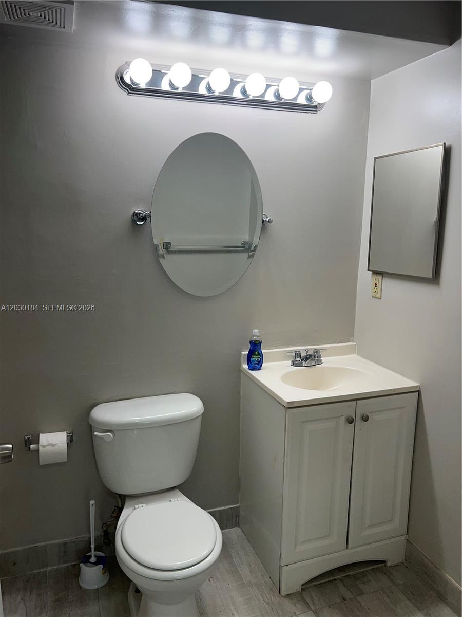 A bathroom features a white vanity, a toilet, an oval mirror, and a vanity light — 951 Lyons Rd # 6104, Coconut Creek FL 33063, COCONUT CREEK, FL