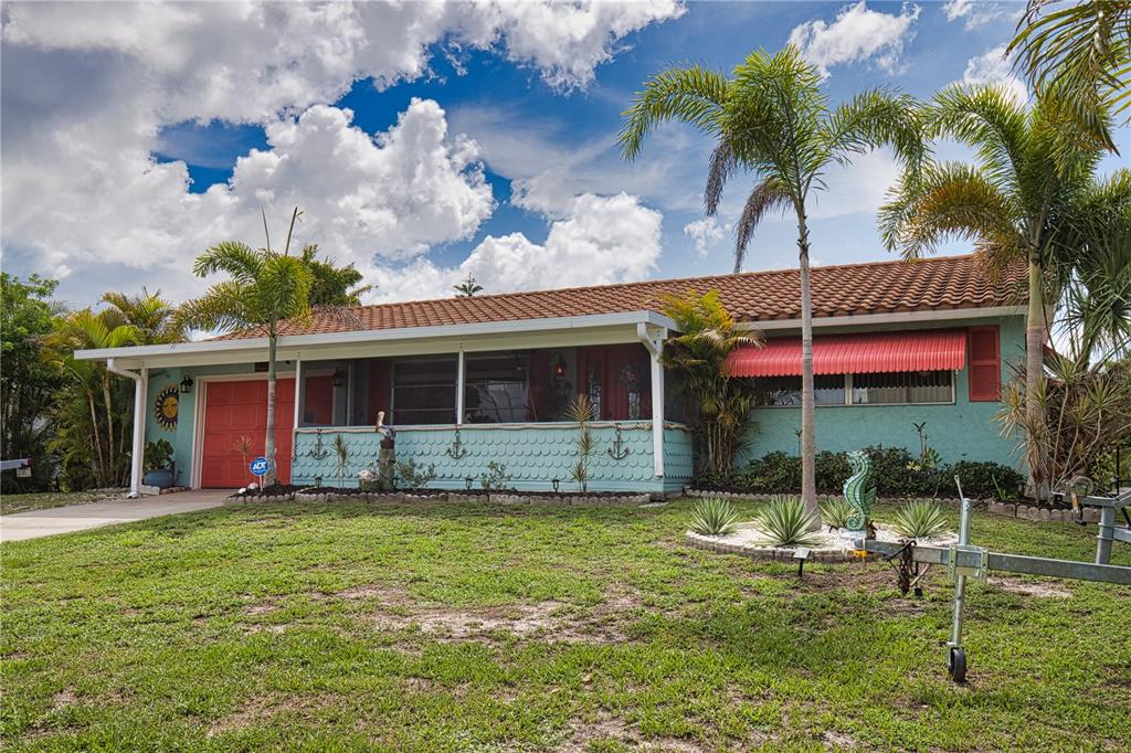 A single-story house with teal siding, a red garage door, and a red window awning — 457 W TARPON BOULEVARD NW, PORT CHARLOTTE, FL