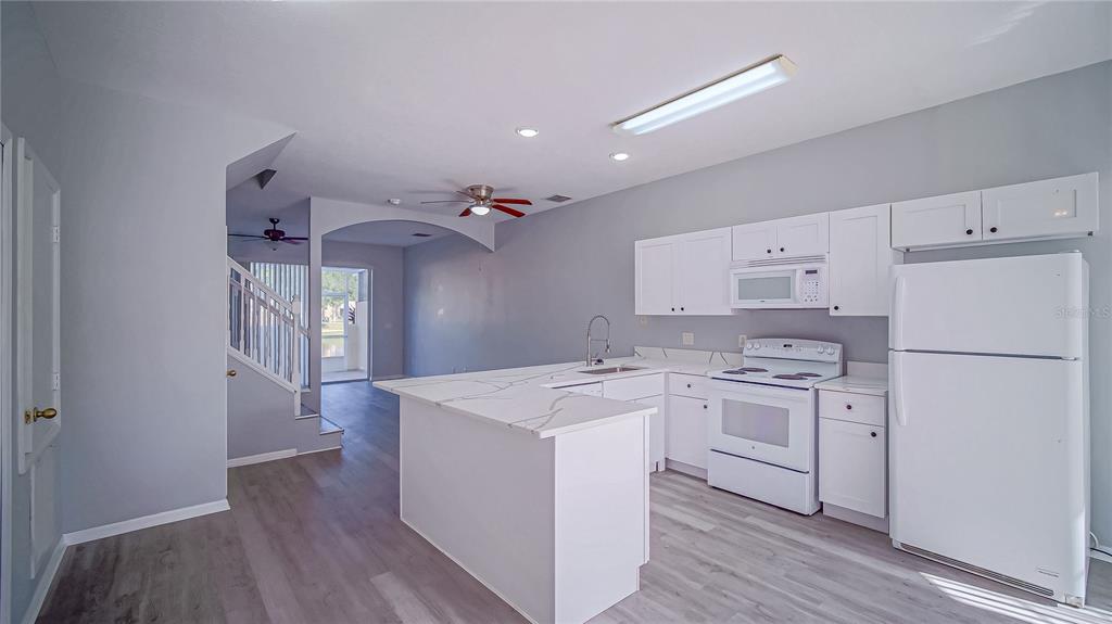 A kitchen with white cabinets, white appliances, and a quartz-topped island overlooks a living area — 1288 S BEACH CIRCLE, KISSIMMEE, FL