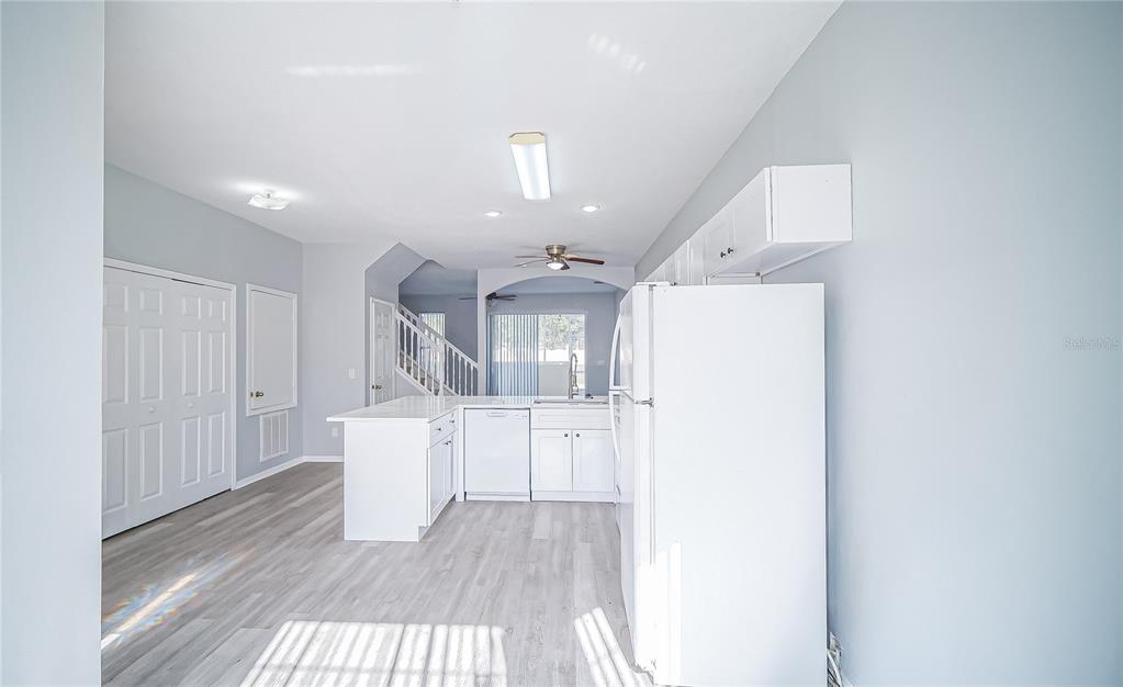 A kitchen with white cabinets, white appliances, and light wood-look flooring opens to a living area — 1288 S BEACH CIRCLE, KISSIMMEE, FL