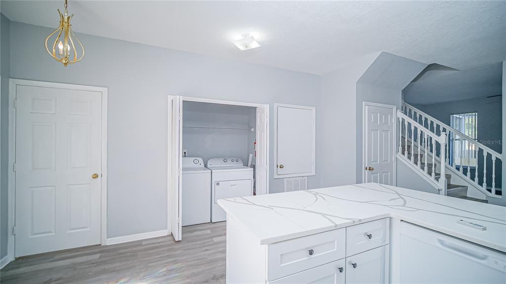 A kitchen island with white cabinets faces a laundry closet and a staircase — 1288 S BEACH CIRCLE, KISSIMMEE, FL
