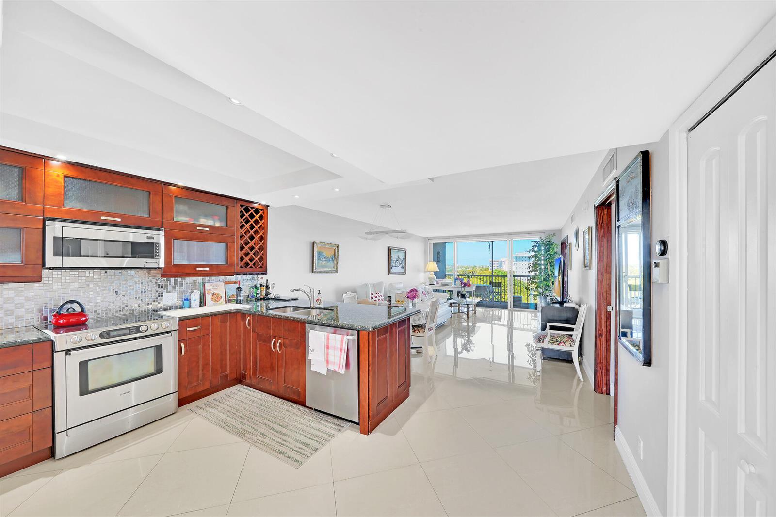 A kitchen with wood cabinets and granite countertops opens into a bright, tiled living area — 2940 N Course Drive # 811, Pompano Beach FL 33069, POMPANO BEACH, FL