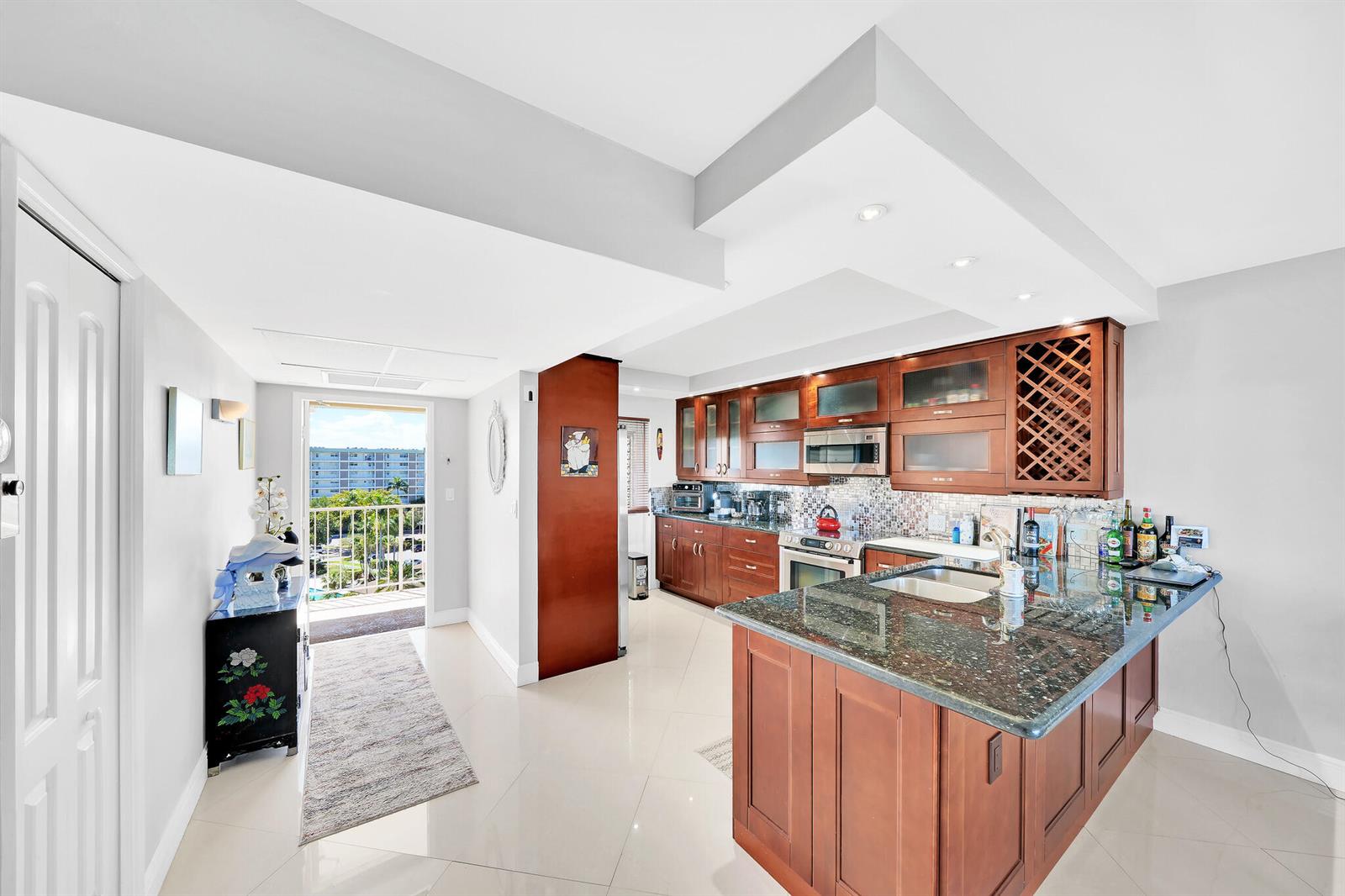 A kitchen with wood cabinets, granite countertops, and an island opens to a balcony view — 2940 N Course Drive # 811, Pompano Beach FL 33069, POMPANO BEACH, FL