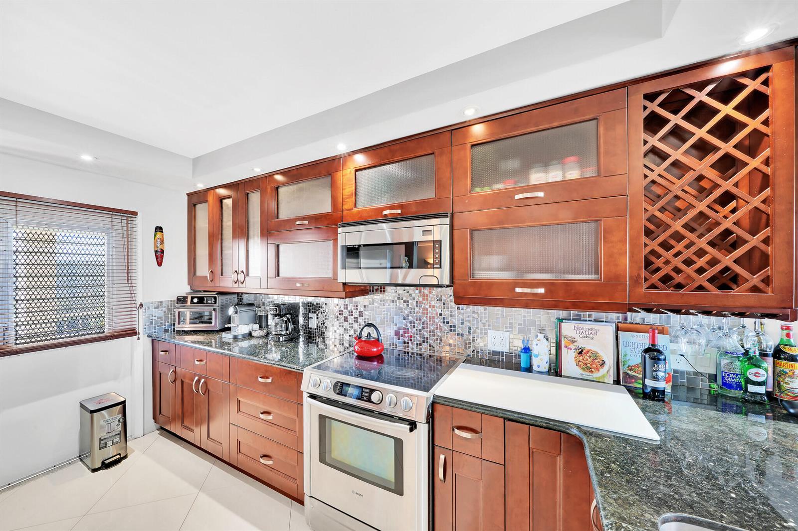 A kitchen with cherry wood cabinets, stainless steel appliances, and a mosaic tile backsplash — 2940 N Course Drive # 811, Pompano Beach FL 33069, POMPANO BEACH, FL