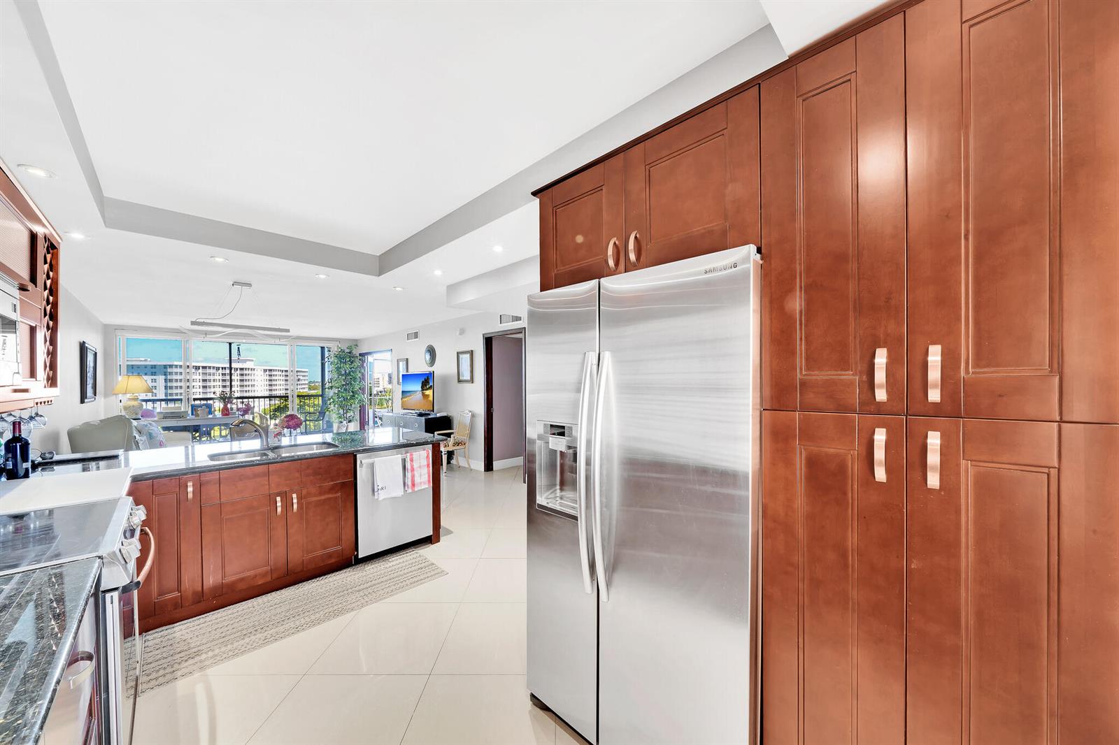 A kitchen with wood cabinets, stainless steel appliances, and tile floors opens to a living area — 2940 N Course Drive # 811, Pompano Beach FL 33069, POMPANO BEACH, FL
